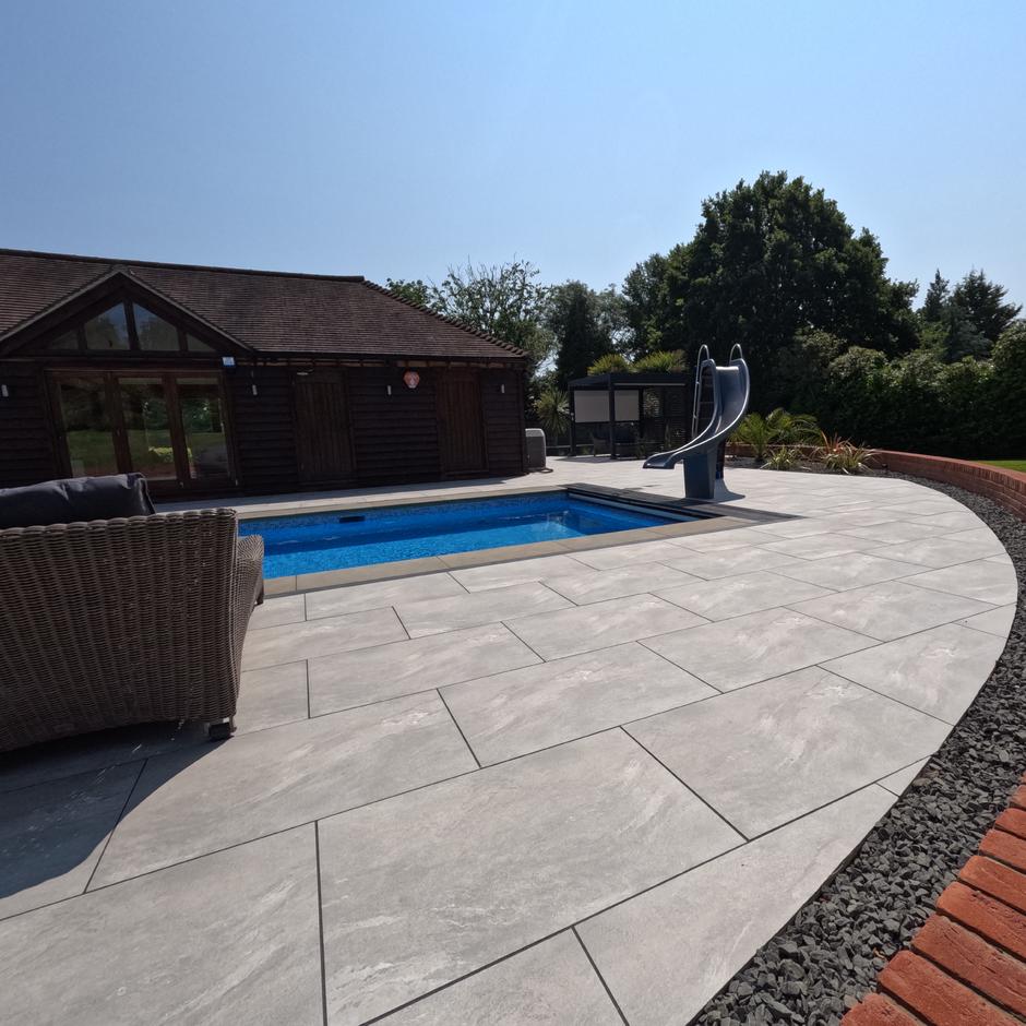 Sienna™ Jupiter Argent Porcelain Paving; grey porcelain slabs; with pool copings and black stone border